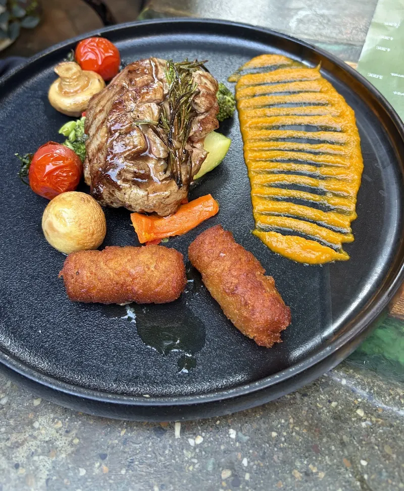 Grilled meat with rosemary, roasted vegetables, croquettes and a pumpkin purée on a dark plate