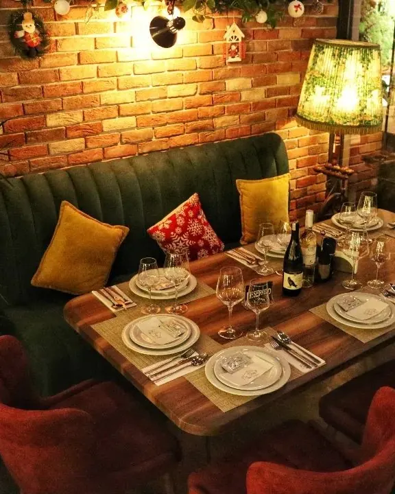 A green velvet banquette and a table set for six under a lamp and a brick wall