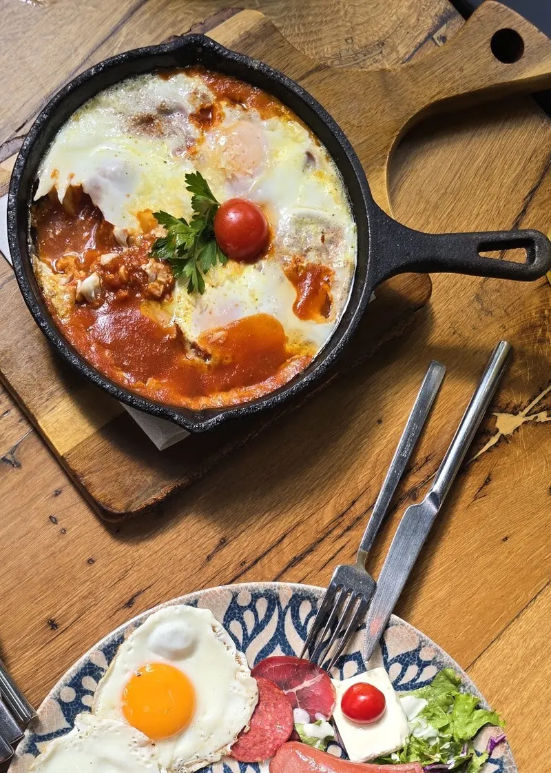 Shakshouka with eggs and cherry tomato in a cast-iron pan, next to a breakfast plate