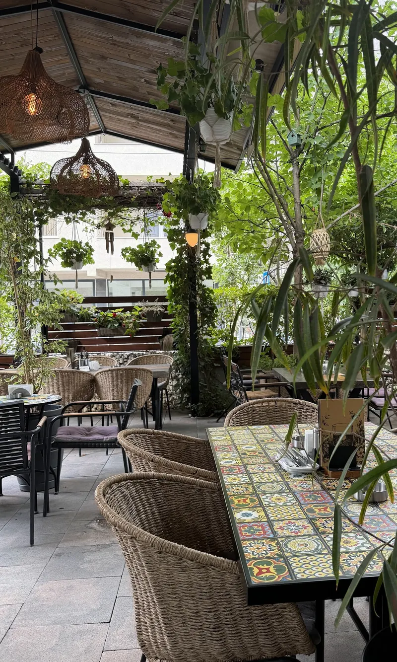 Wicker chairs and a tiled table on the garden terrace, under hanging plants and woven lamps